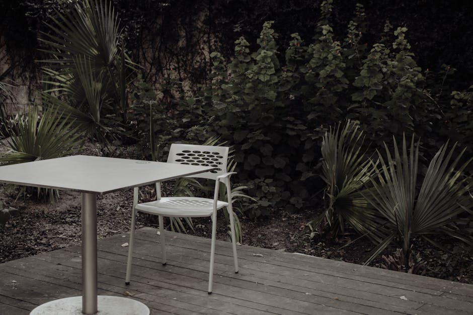 A tranquil outdoor setting with a modern chair and table, surrounded by lush green plants.